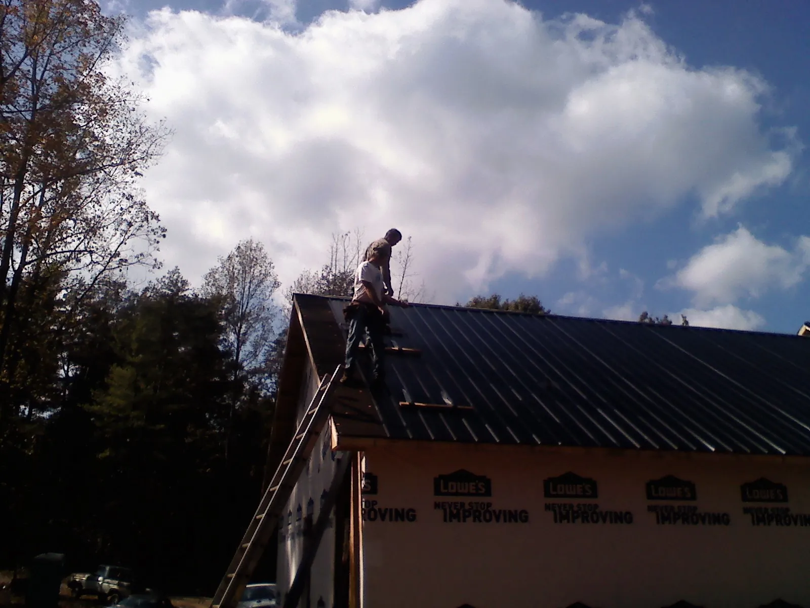 Roofer fastening dark metal panels high against a cloudy sky, from a Roof Inspection job in Candor