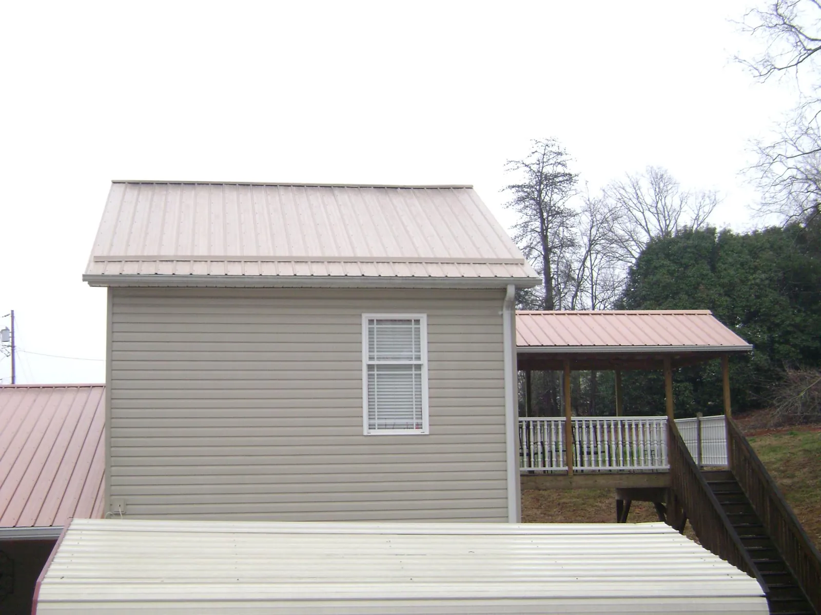 Tan metal roofs on a two story addition and attached porch, from a Roof Replacement job in Candor